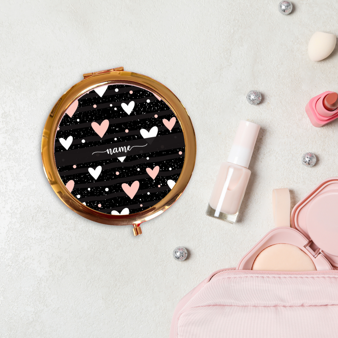 Round compact mirror with heart design on a light surface with makeup items.