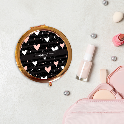 Round compact mirror with heart design on a light surface with makeup items.